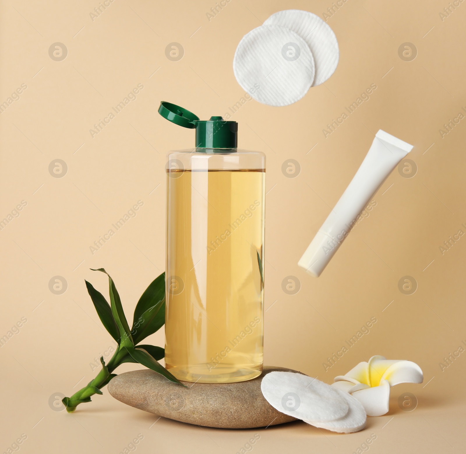 Photo of Tube of cream and cotton pads flying near bottle of micellar water on beige background