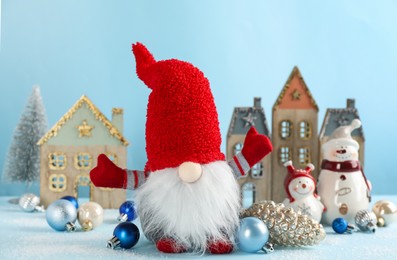 Photo of Cute Christmas gnome and festive decor on light blue background