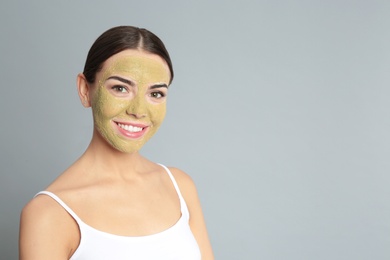 Photo of Young woman with clay mask on her face against grey background, space for text. Skin care