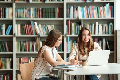 Photo of Young women discussing group project at table in library