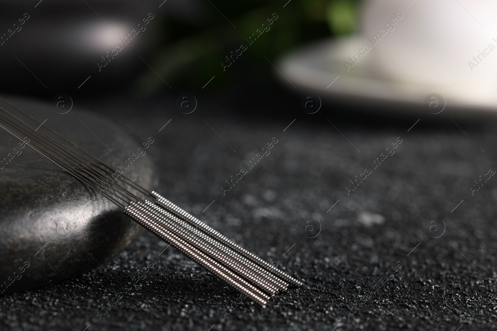 Photo of Acupuncture needles and spa stone on black textured table, closeup. Space for text