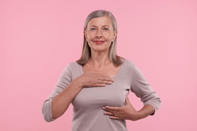 Photo of Beautiful senior woman doing breast self-examination on pink background