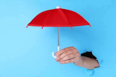 Woman holding open small red umbrella through hole in light blue paper, closeup