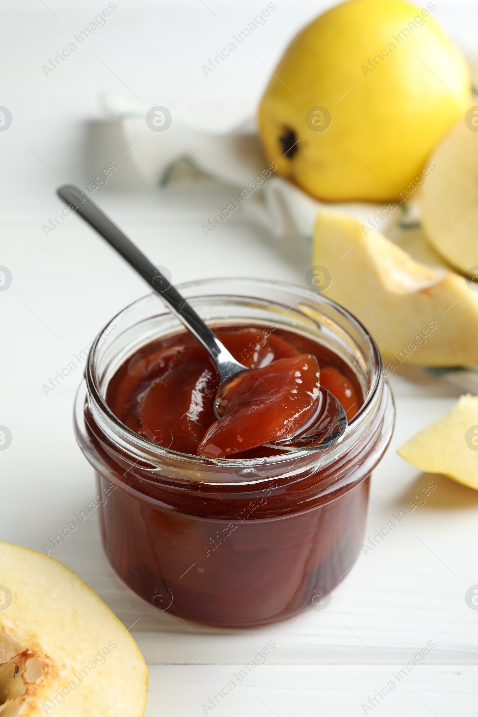 Photo of Tasty homemade quince jam in jar, spoon and fruits on white wooden table