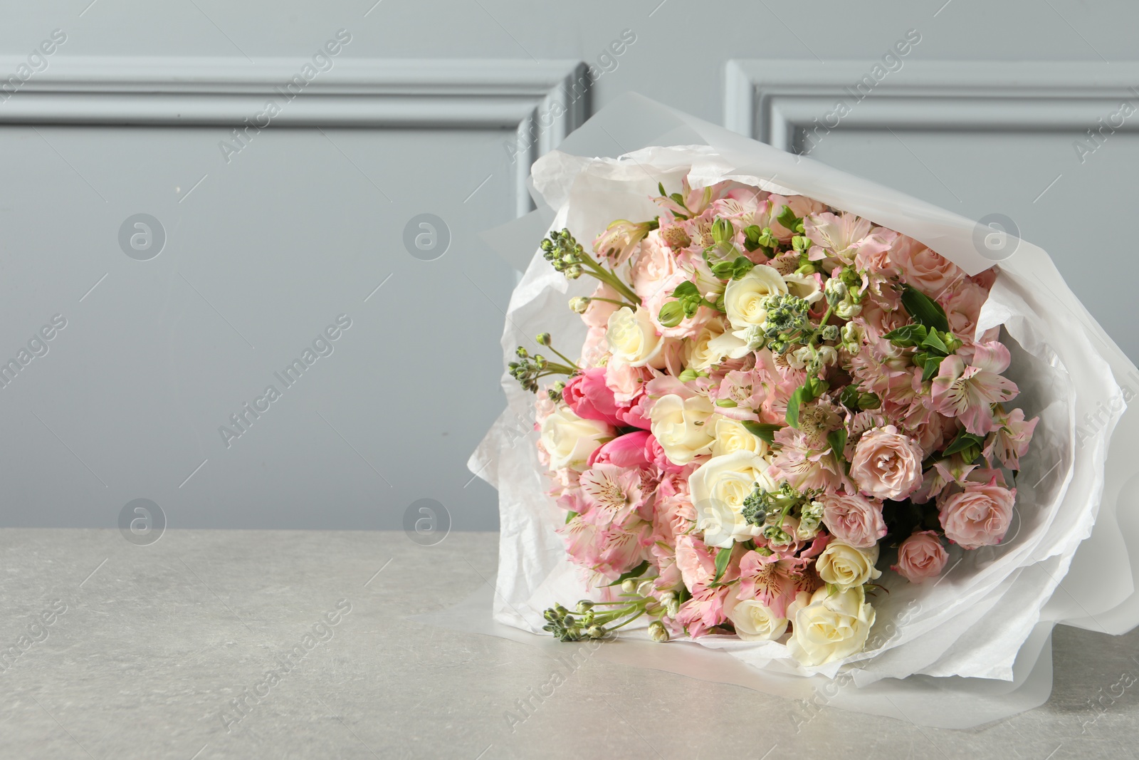 Photo of Beautiful bouquet of fresh flowers on table near grey wall, space for text