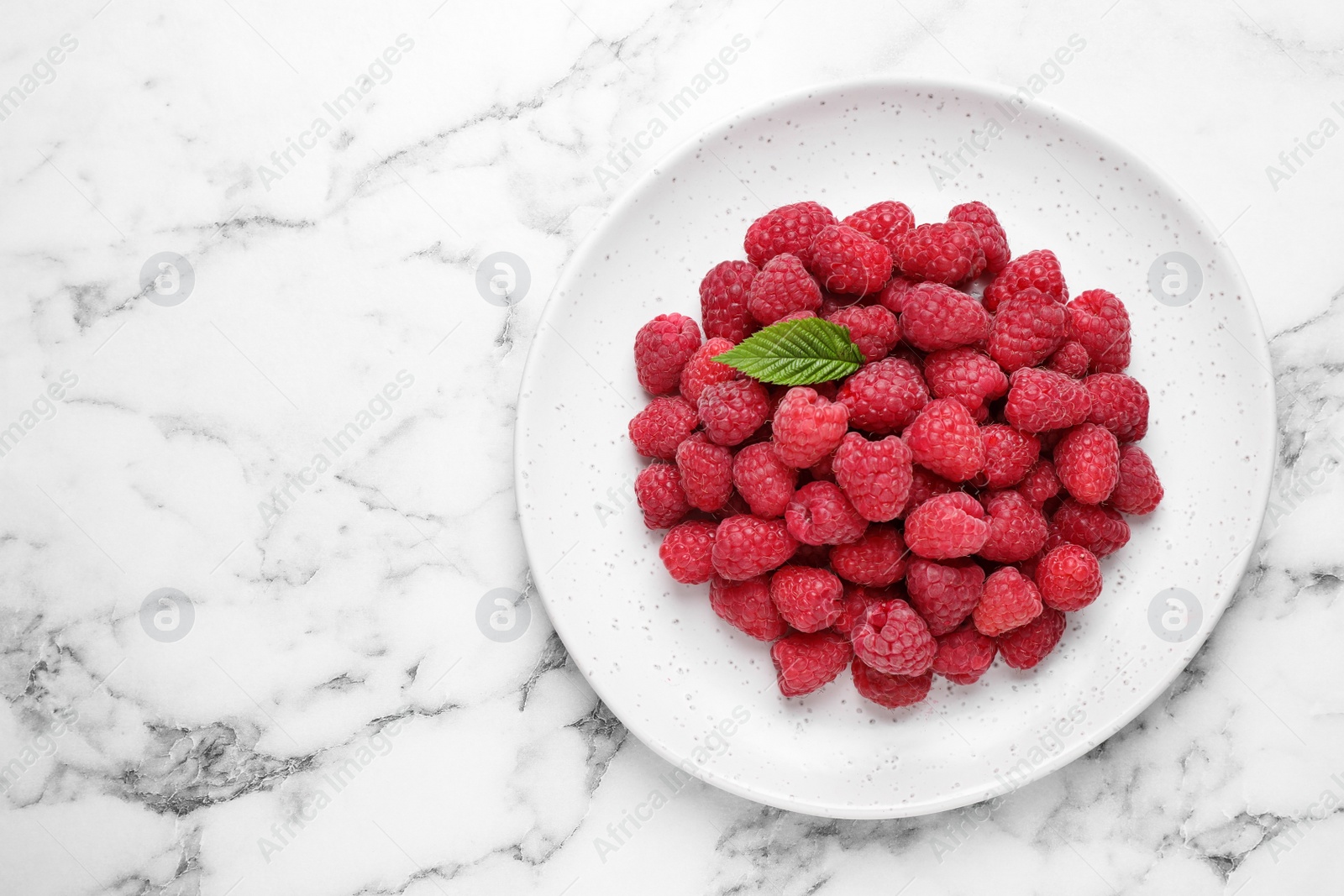 Photo of Delicious fresh ripe raspberries in plate on white marble table, top view. Space for text