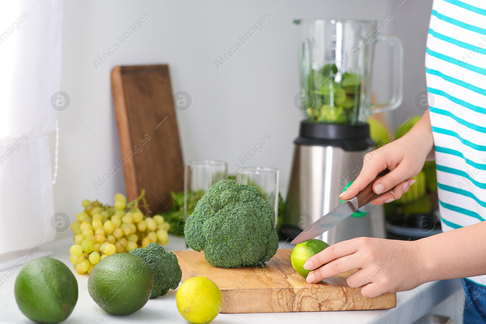 Photo of Woman cutting lime for smoothie in kitchen, closeup