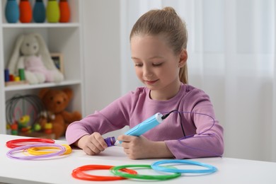 Girl drawing with stylish 3D pen at white table indoors