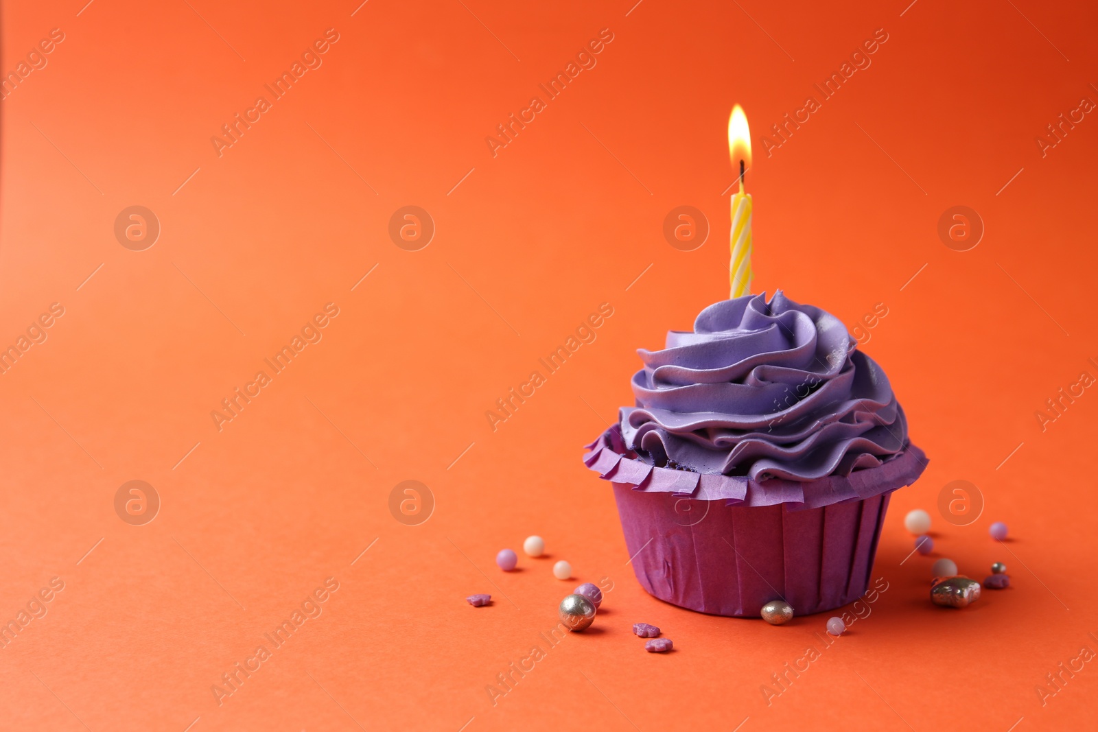 Photo of Delicious birthday cupcake with burning candle and sprinkles on coral background. Space for text