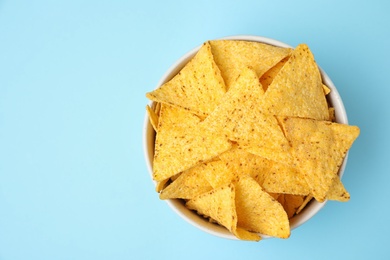 Bowl with tasty Mexican nachos chips on light blue background, top view. Space for text