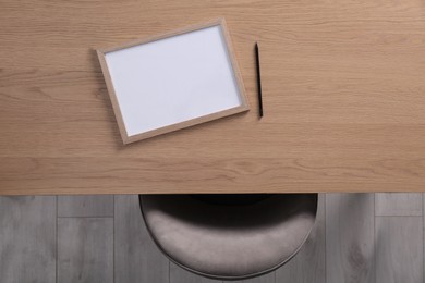 Photo of Chair near wooden table with blank frame and pencil indoors, top view. Mockup for design