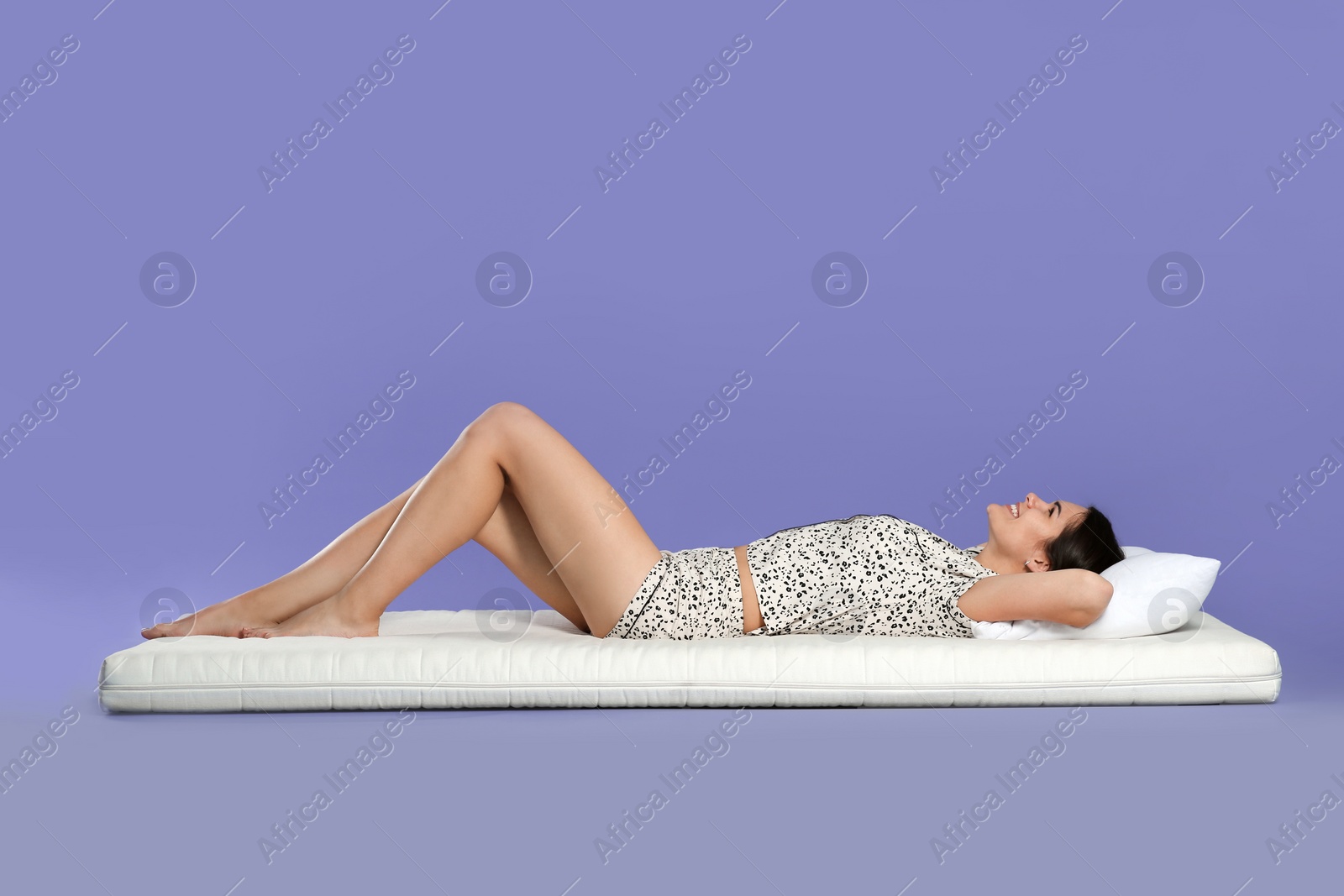 Photo of Young woman lying on soft mattress against light purple background