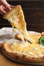 Photo of Woman taking piece of delicious cheese pizza at wooden table, closeup