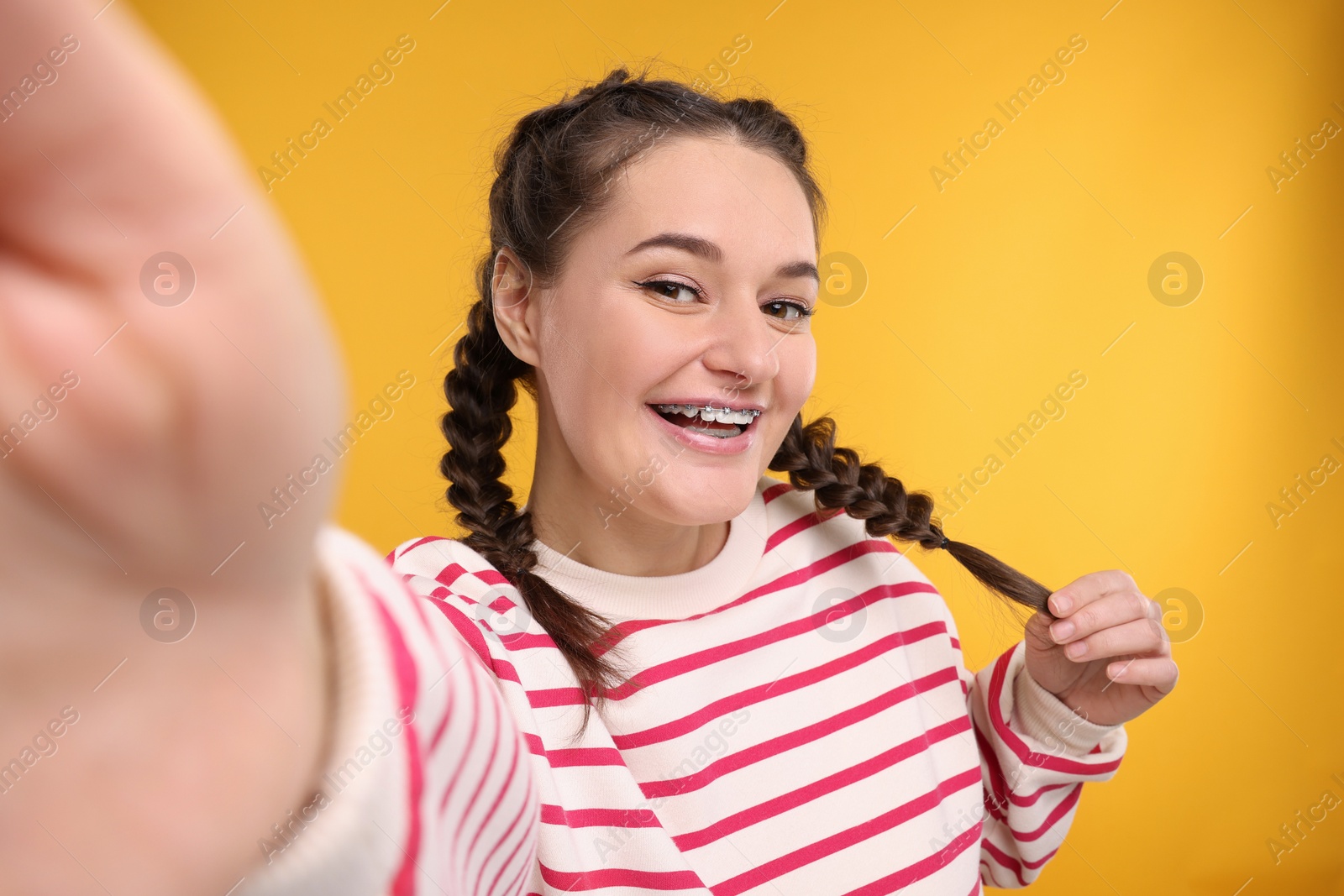 Photo of Smiling woman with braces taking selfie on orange background