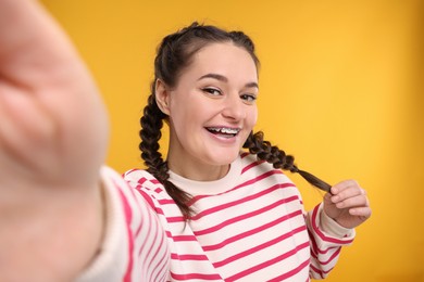 Smiling woman with braces taking selfie on orange background