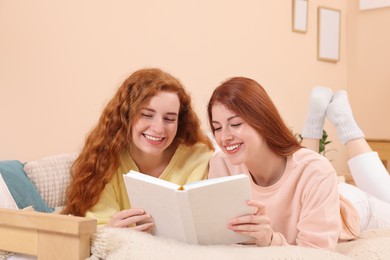 Photo of Beautiful young sisters reading book on bed at home