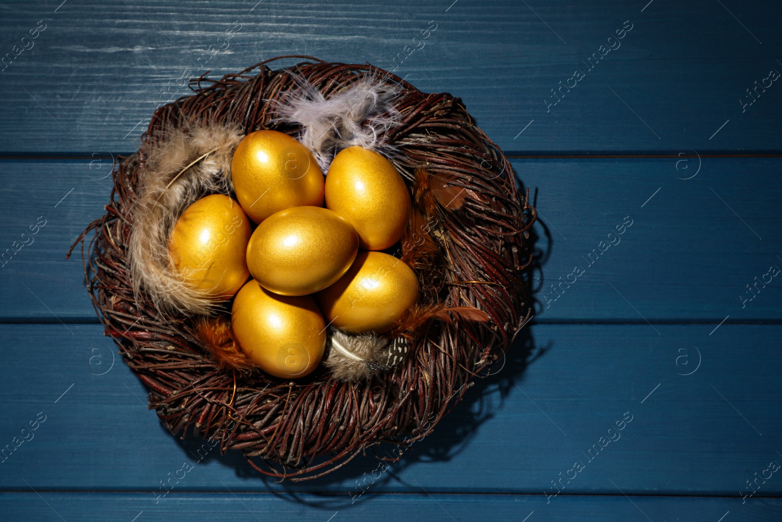 Photo of Nest with golden eggs on blue wooden table, top view. Space for text