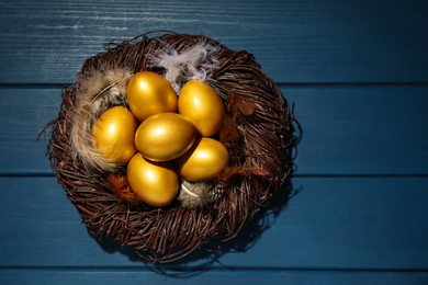 Photo of Nest with golden eggs on blue wooden table, top view. Space for text
