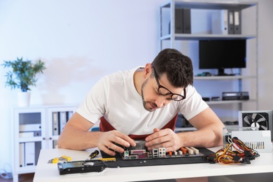Photo of Male technician repairing motherboard at table indoors