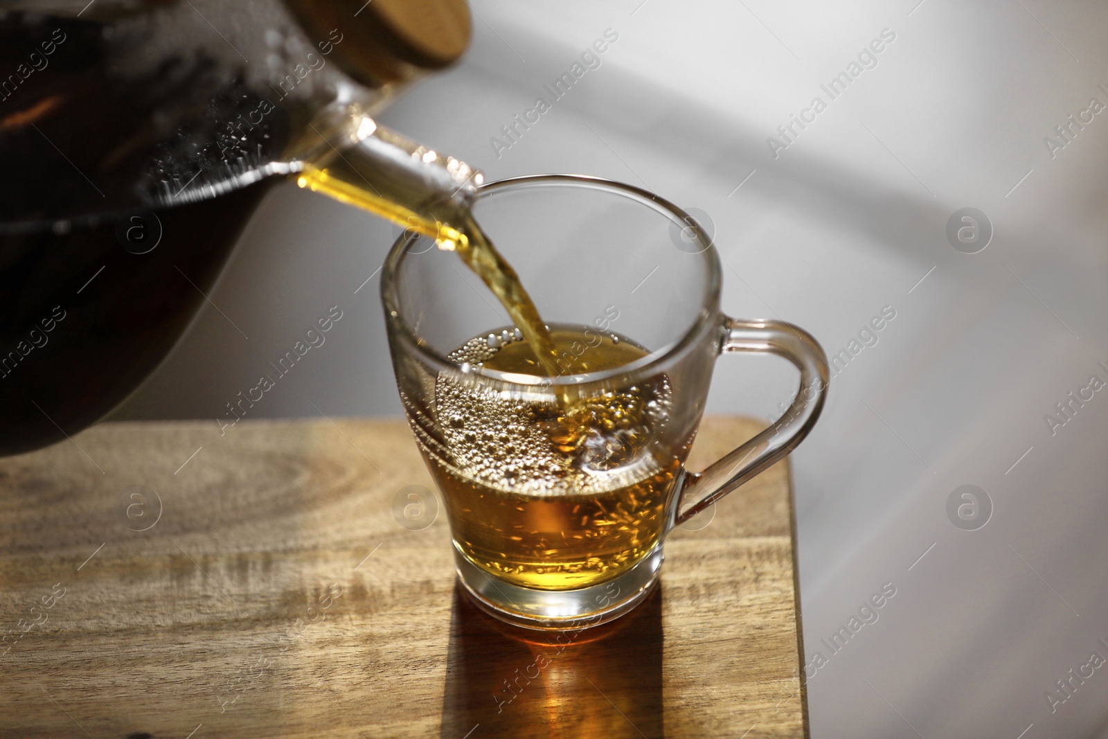 Photo of Pouring delicious tea into glass cup on wooden table, closeup