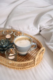 Photo of Wicker tray with cup of coffee and candles near soft blanket on bed