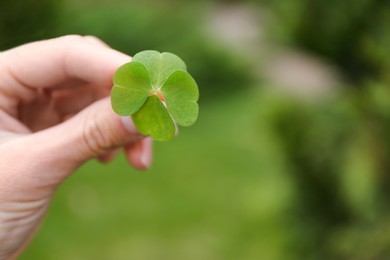 Photo of Woman holding beautiful green four leaf clover outdoors, closeup. Space for text