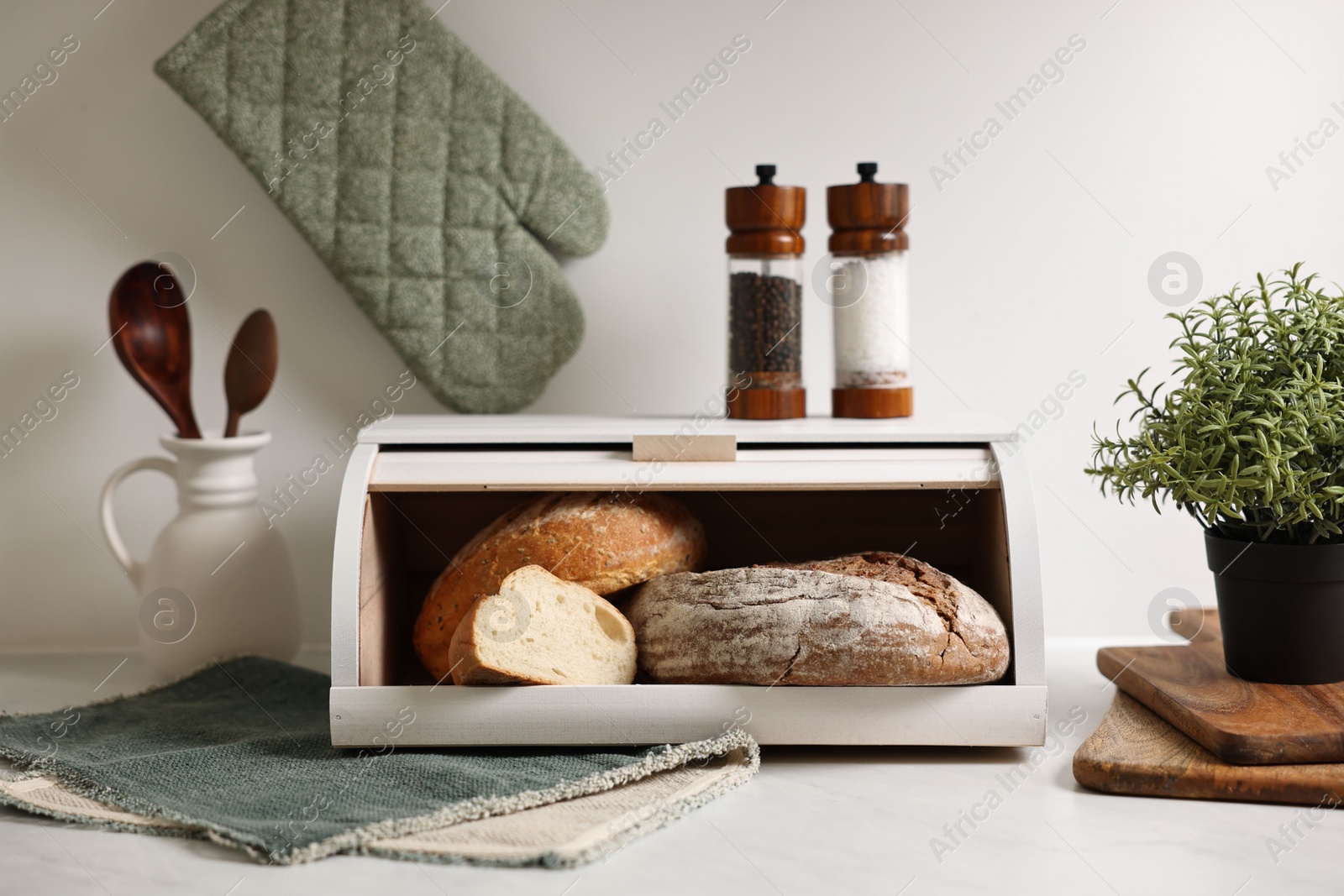 Photo of Wooden bread basket with freshly baked loaves on white marble table in kitchen