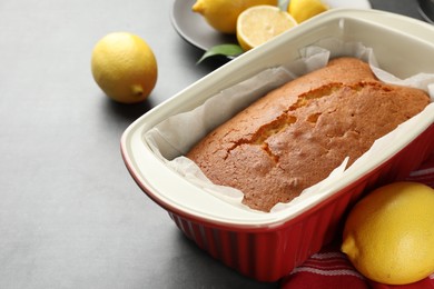 Photo of Tasty lemon cake in baking dish and citrus fruits on grey table, closeup. Space for text