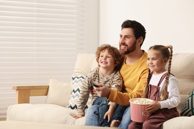 Photo of Happy father and children watching TV with popcorn on sofa indoors, space for text