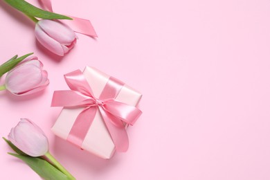 Beautiful gift box and tulips on pink background, flat lay. Space for text