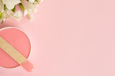 Photo of Wooden spatula, hot depilatory wax and flowers on light pink background, flat lay. Space for text