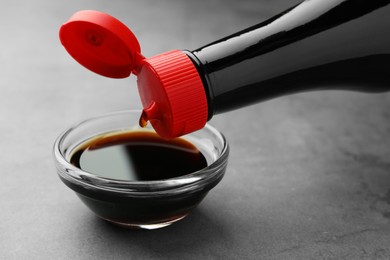 Photo of Pouring soy sauce into bowl on grey table, closeup