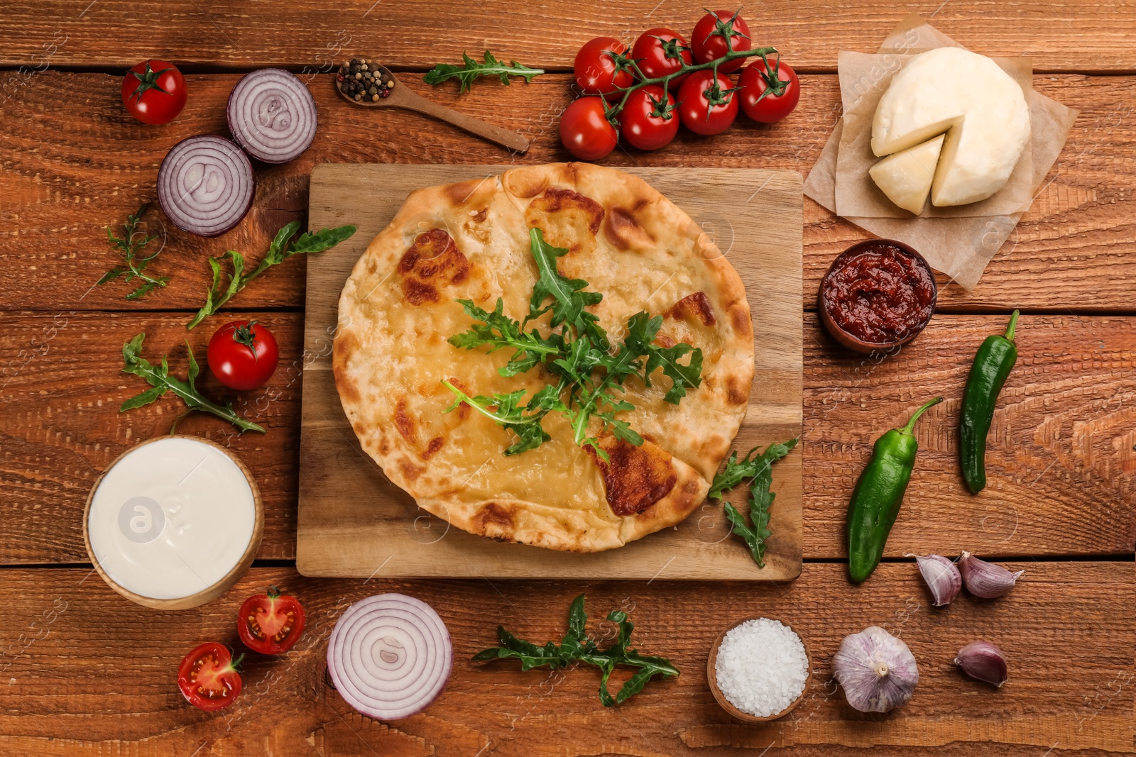 Photo of Delicious khachapuri with cheese, sauces, vegetables and spices on wooden table, flat lay