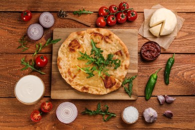 Delicious khachapuri with cheese, sauces, vegetables and spices on wooden table, flat lay