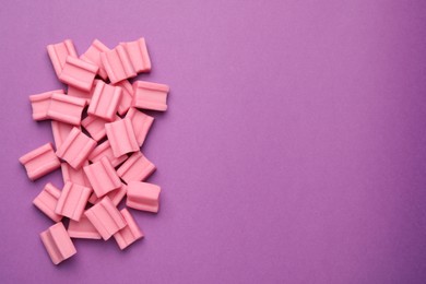 Photo of Tasty pink chewing gums on purple background, flat lay. Space for text