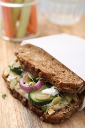 Photo of Tasty vegan sandwich with cucumber, onion, hummus and pumpkin seeds on wooden board, closeup