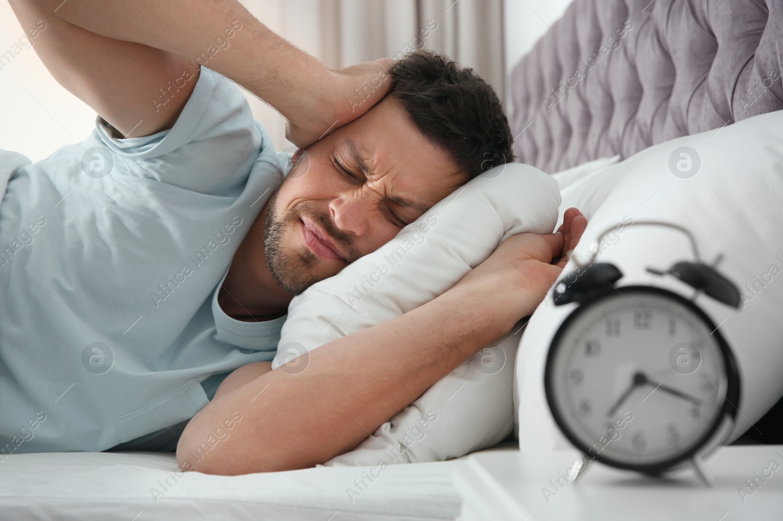 Photo of Sleepy man closing ears at home in morning