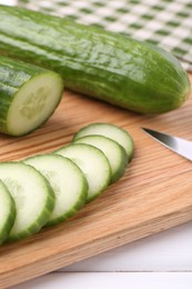 Fresh cucumbers and knife on wooden cutting board, closeup