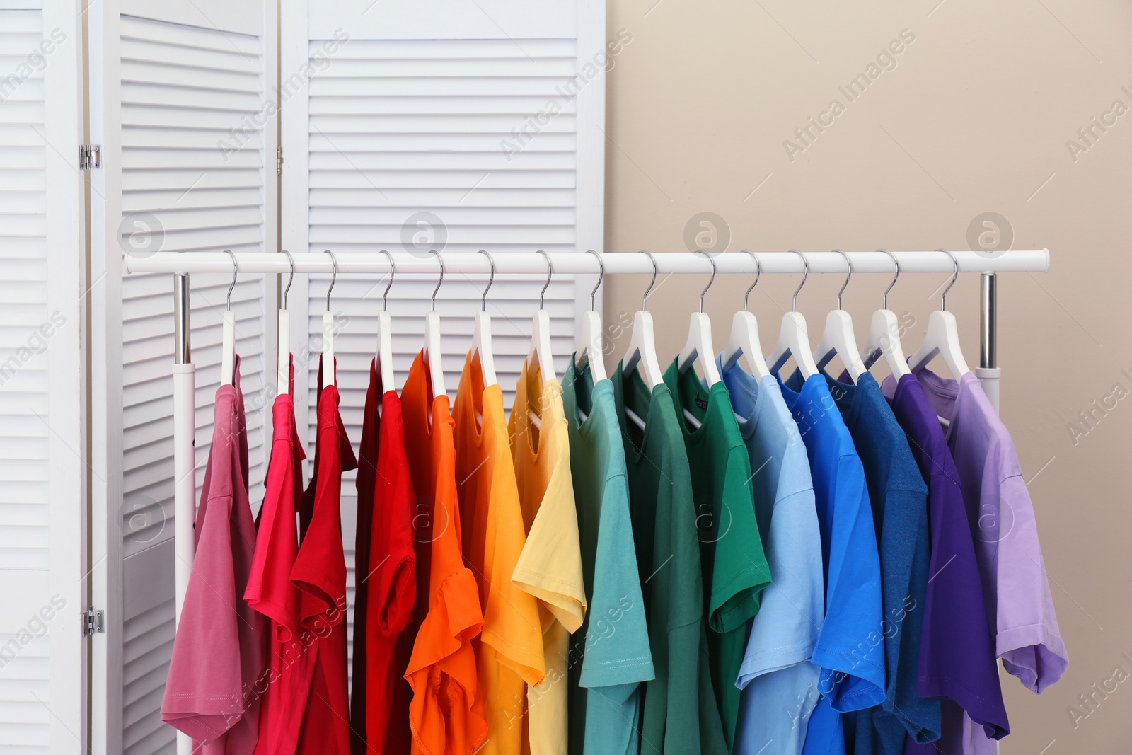 Photo of Rack with bright clothes in room. Rainbow colors