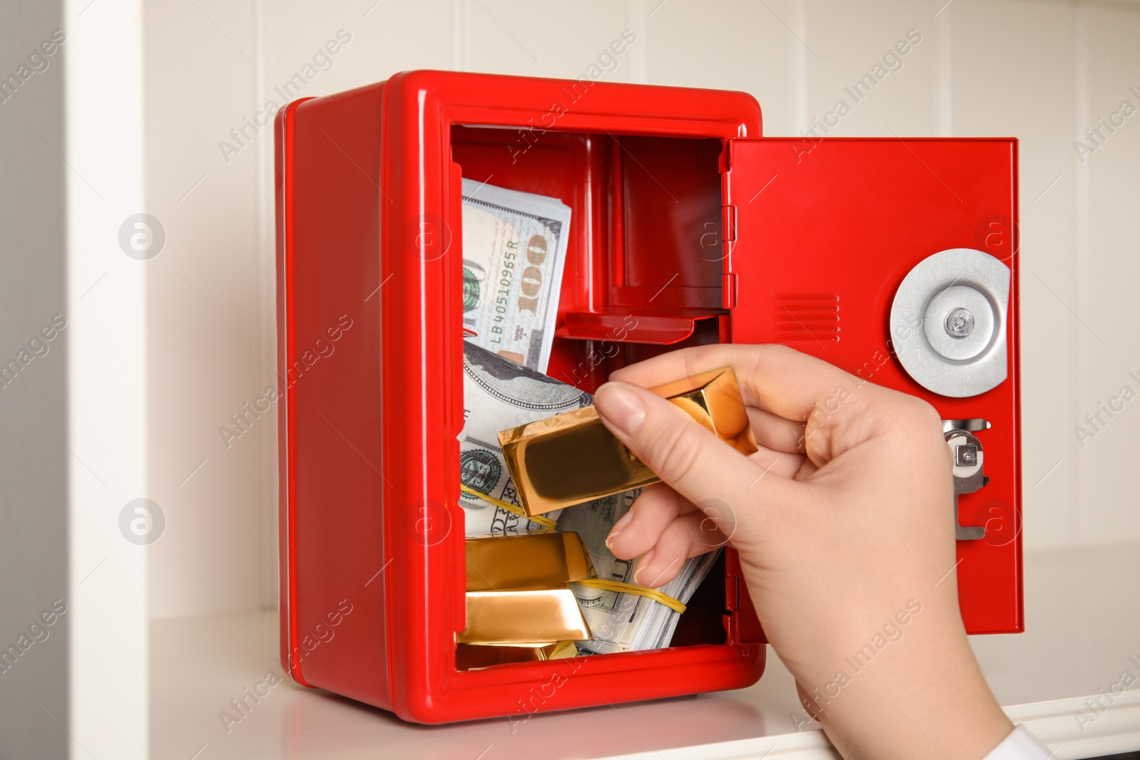 Woman putting gold bar into red steel safe, closeup Photo of Woman putting gold bar into red steel safe, closeup
