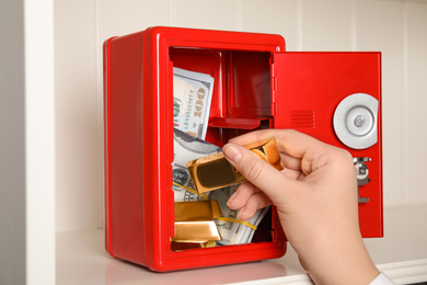 Photo of Woman putting gold bar into red steel safe, closeup