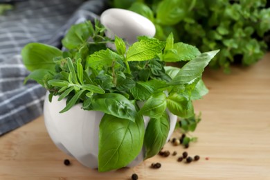 Photo of Mortar with different fresh herbs and black peppercorns on wooden table, closeup
