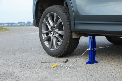 Photo of Car lifted by scissor jack without wheel outdoors, closeup. Tire puncture