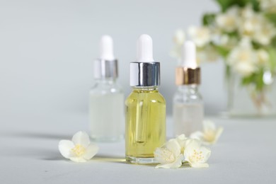 Photo of Essential oils in bottles and beautiful jasmine flowers on grey background, closeup