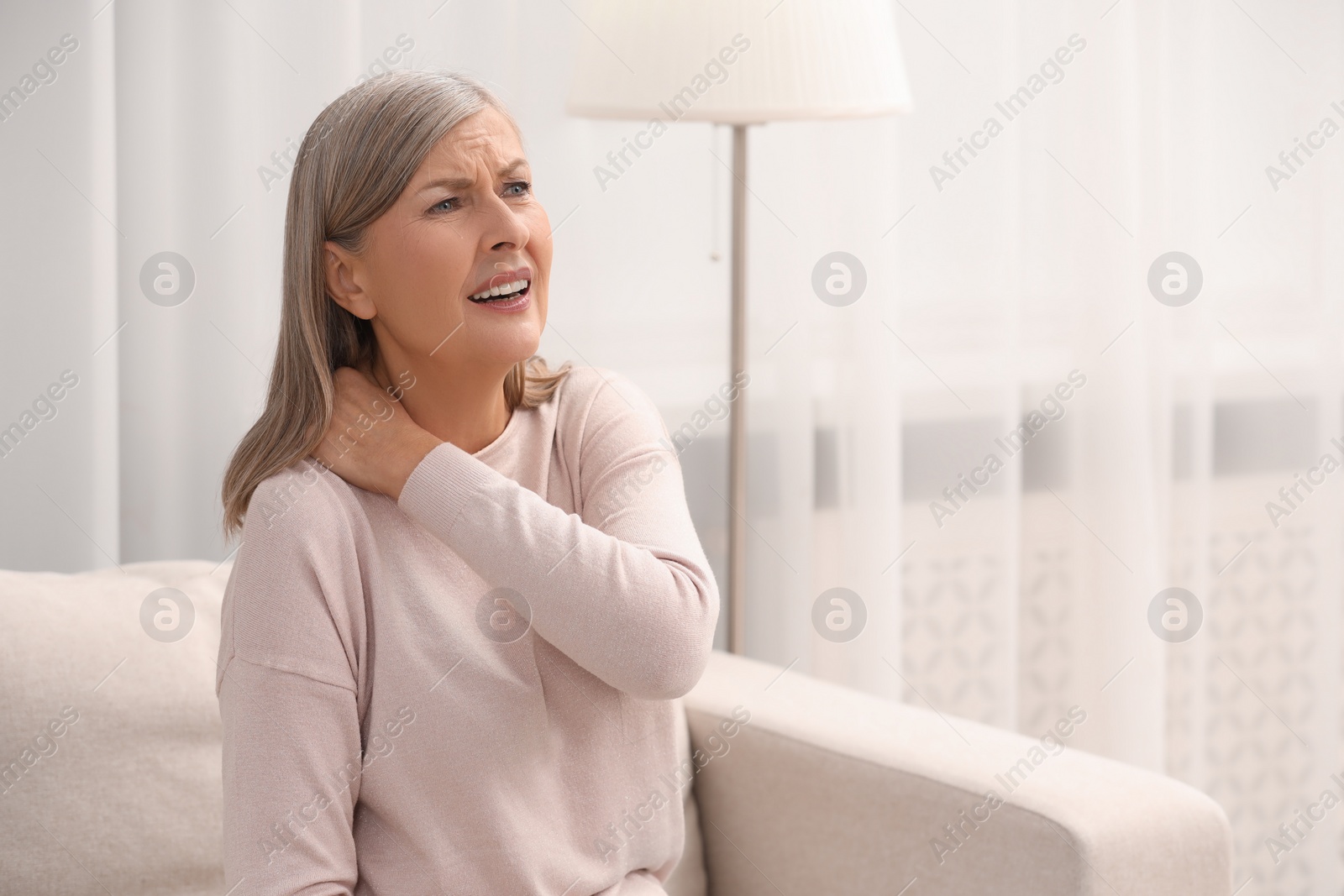 Photo of Mature woman suffering from pain in neck at home. Rheumatism symptom