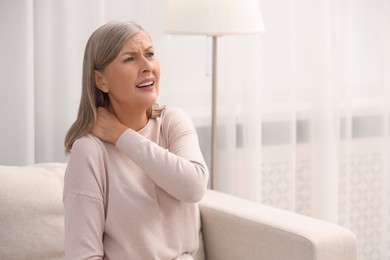 Photo of Mature woman suffering from pain in neck at home. Rheumatism symptom