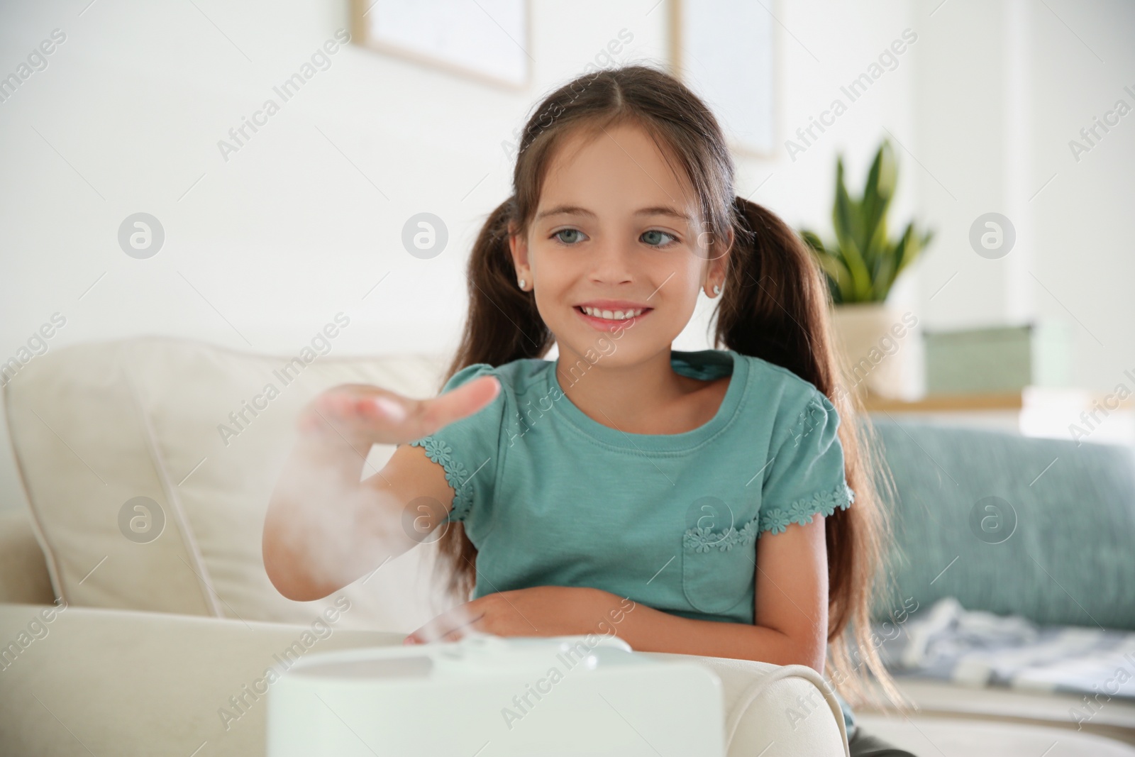 Photo of Little girl near modern air humidifier at home