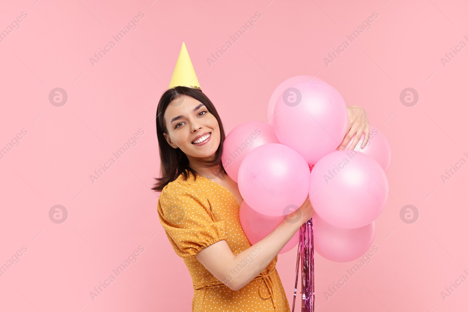 Photo of Happy young woman in party hat with balloons on pink background