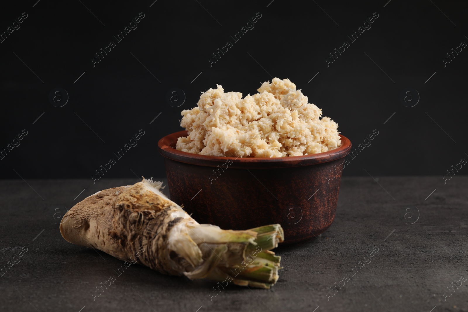 Photo of Bowl of tasty prepared horseradish and root on grey table