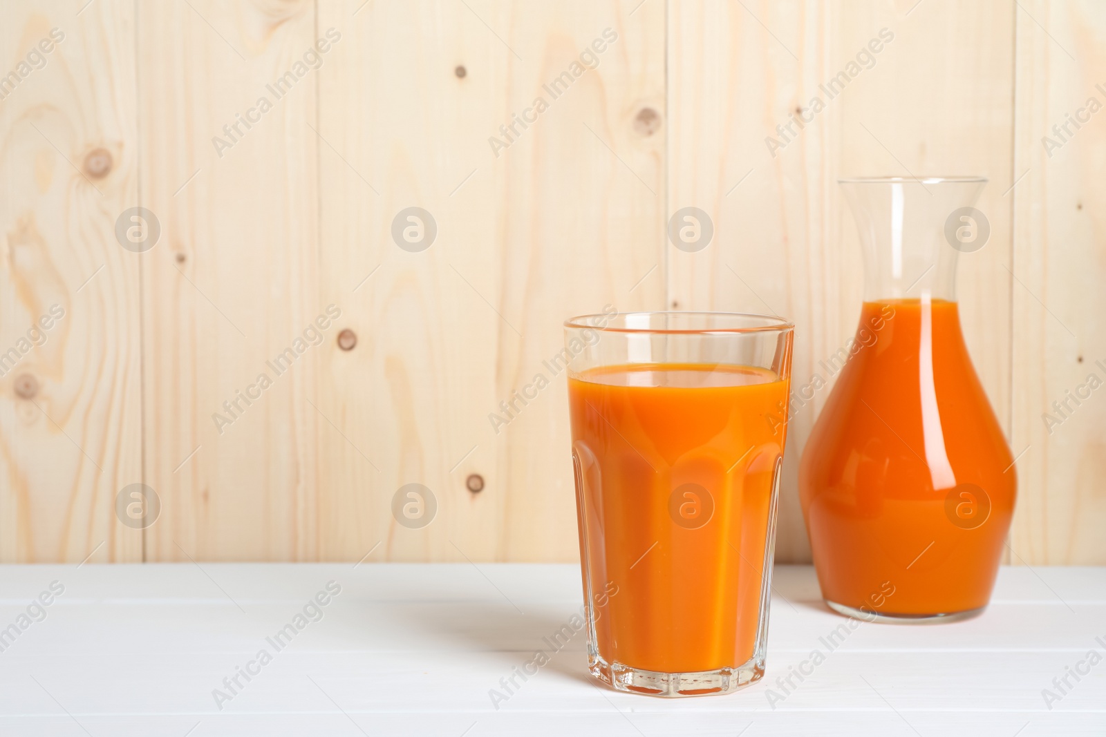 Photo of Tasty carrot juice on white wooden table, space for text